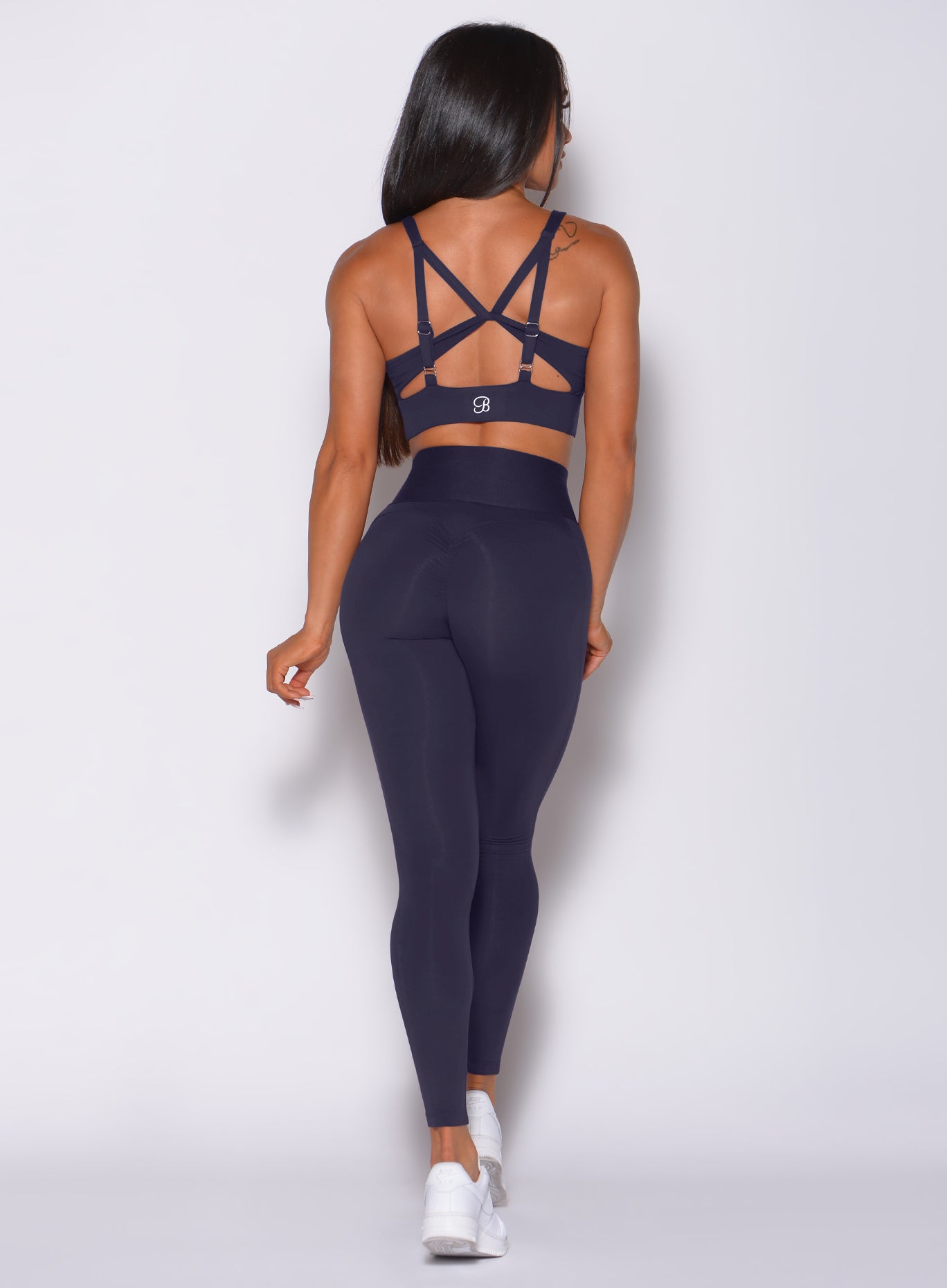 Back profile view of a model in our waist cincher leggings in twilight blue color and a matching bra