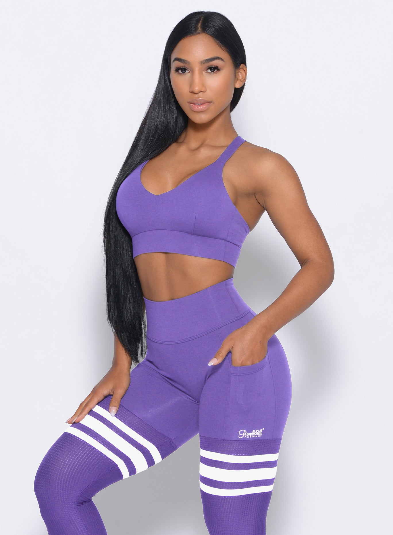 Left side view of the model angled left wearing our synergy sports bra in royal purple color and a matching leggings