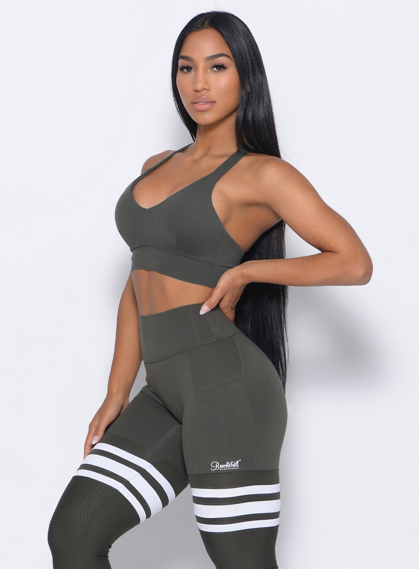 Left side view of the model in our synergy sports bra in hunter green color and a matching leggings