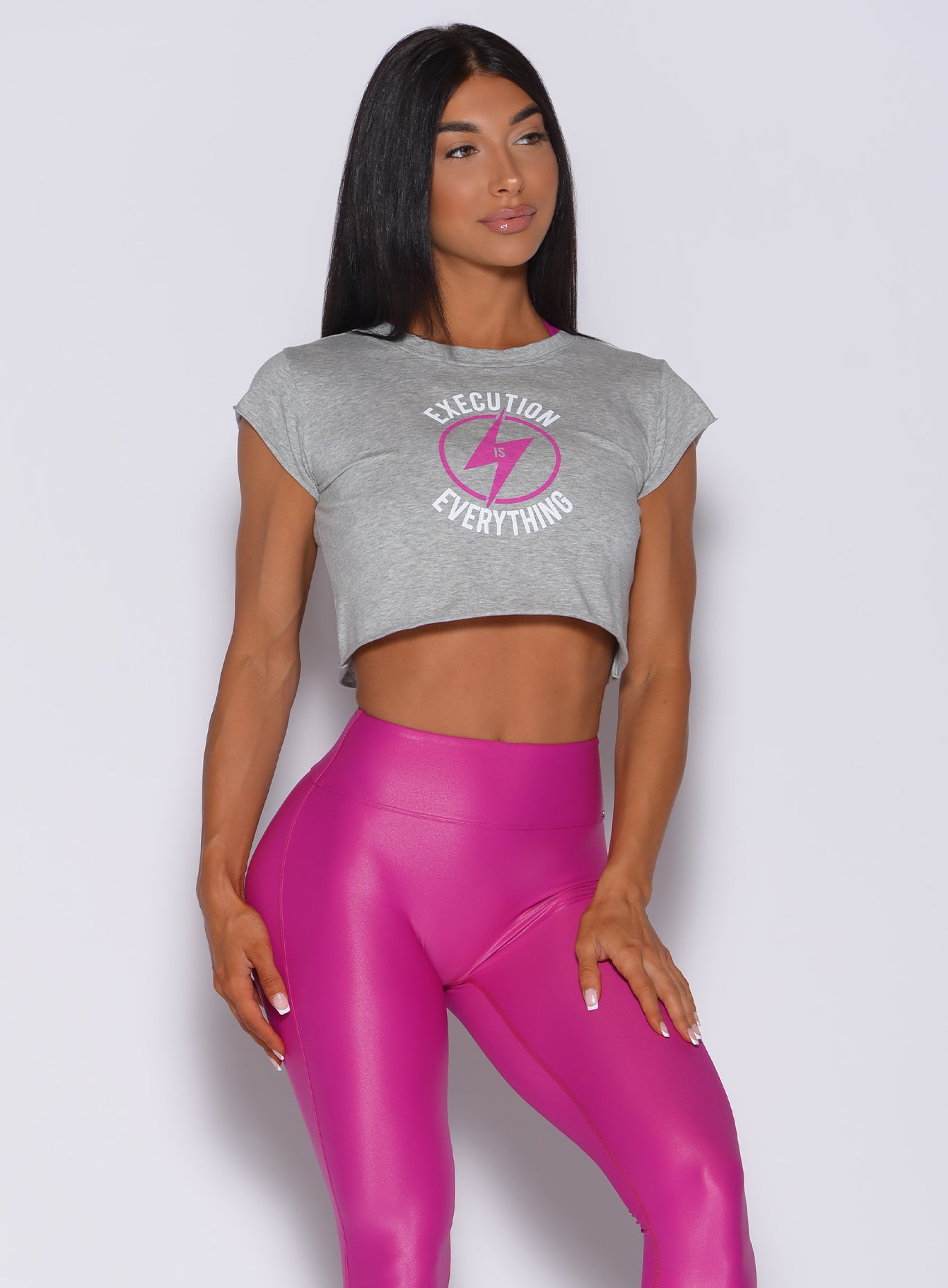 Front profile view of a model in our execution tee in heather gray color and a pink gloss leggings