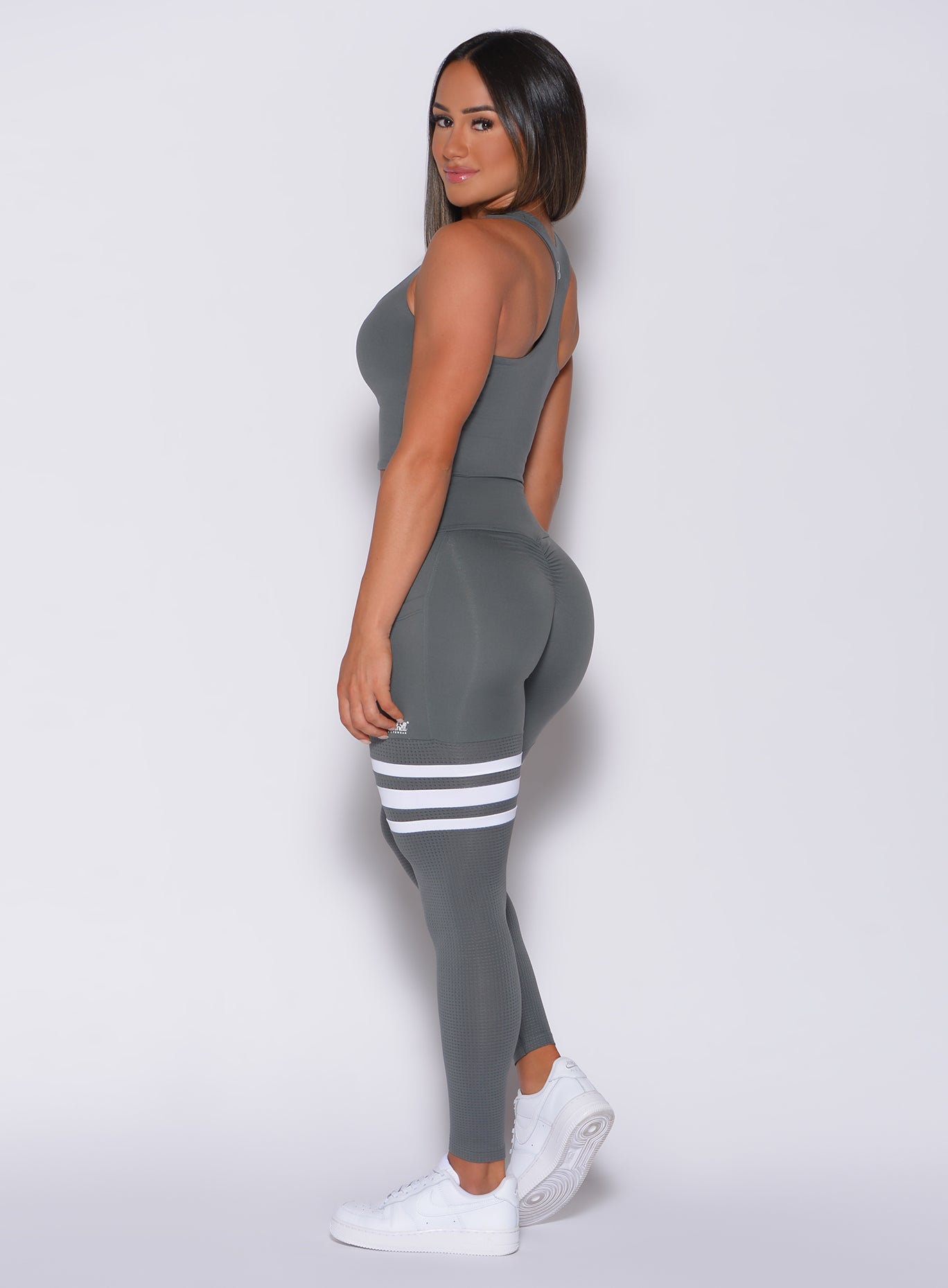 Left side profile view of a model in our scrunch thigh high in steel gray color and a matching sports bra