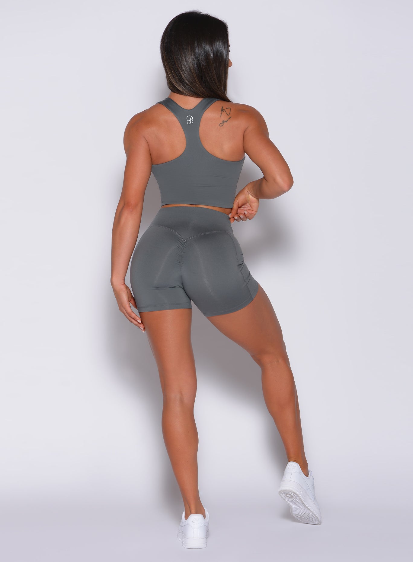 Back profile view of a model in our tiny waist shorts in steel gray color and a matching bra