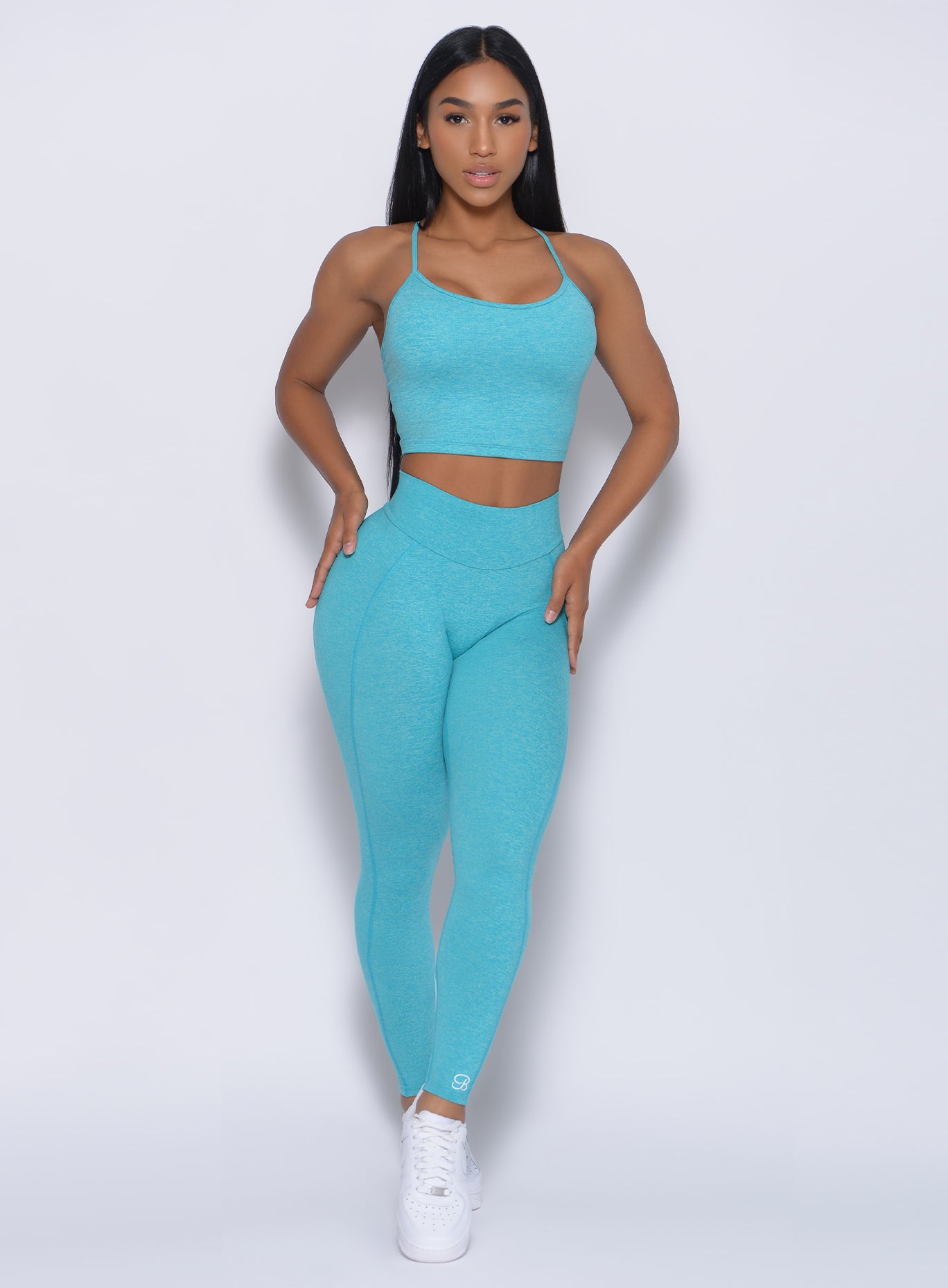 Front profile view of a model with her hands on waist wearing our relax sports bra in crystal blue color and a matching leggings