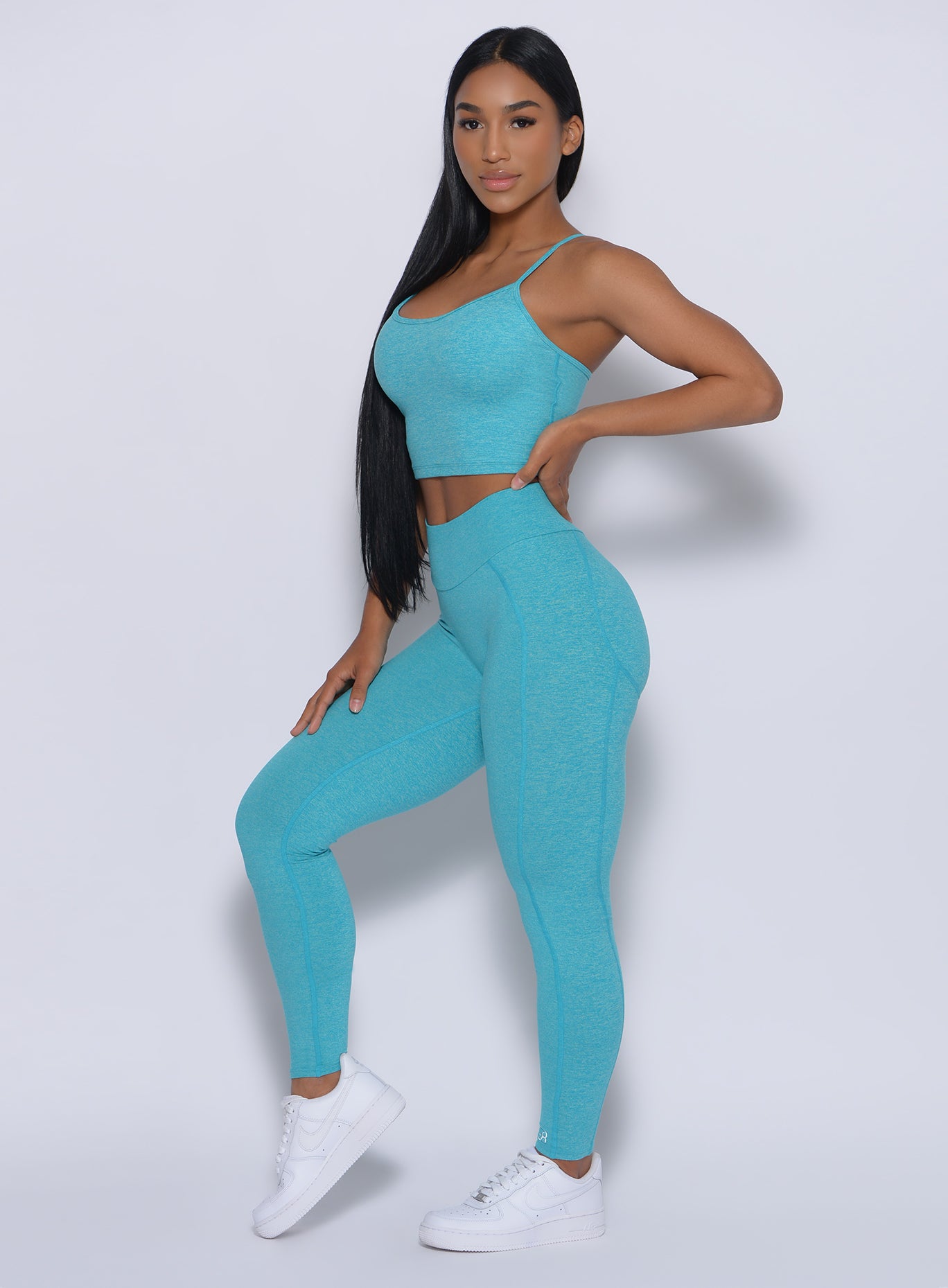 Right side view of a model with her left hand on waist wearing our uplift leggings in crystal blue color and a matching bra 