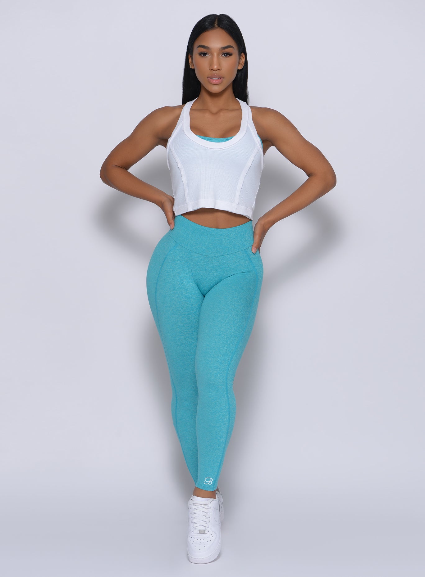 Front profile view of a model with her hands on waist wearing our white rib crop tank and a blue leggings 