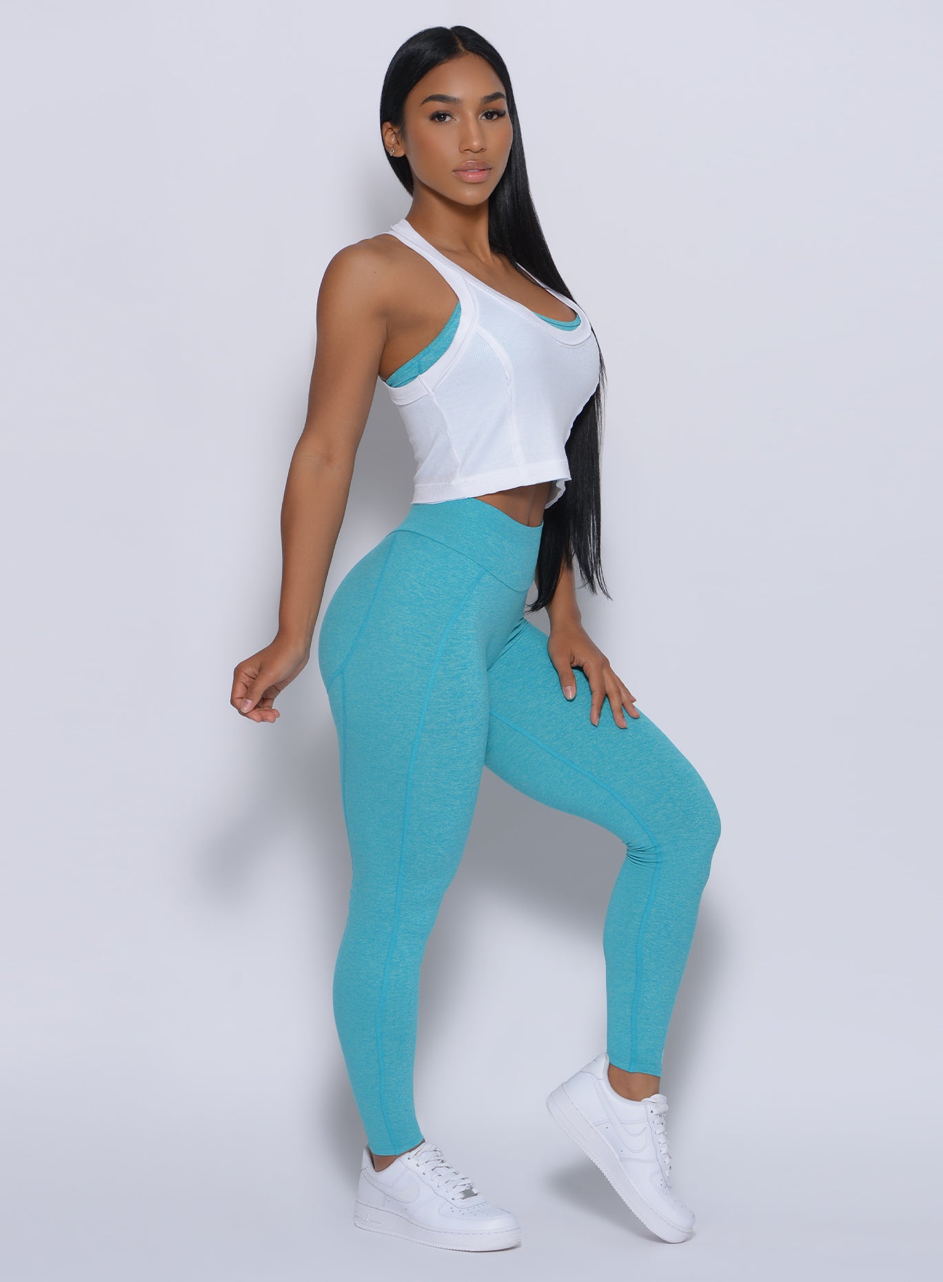 Right side view of a model angled right wearing our white rib crop tank over a blue bra and a matching leggings 