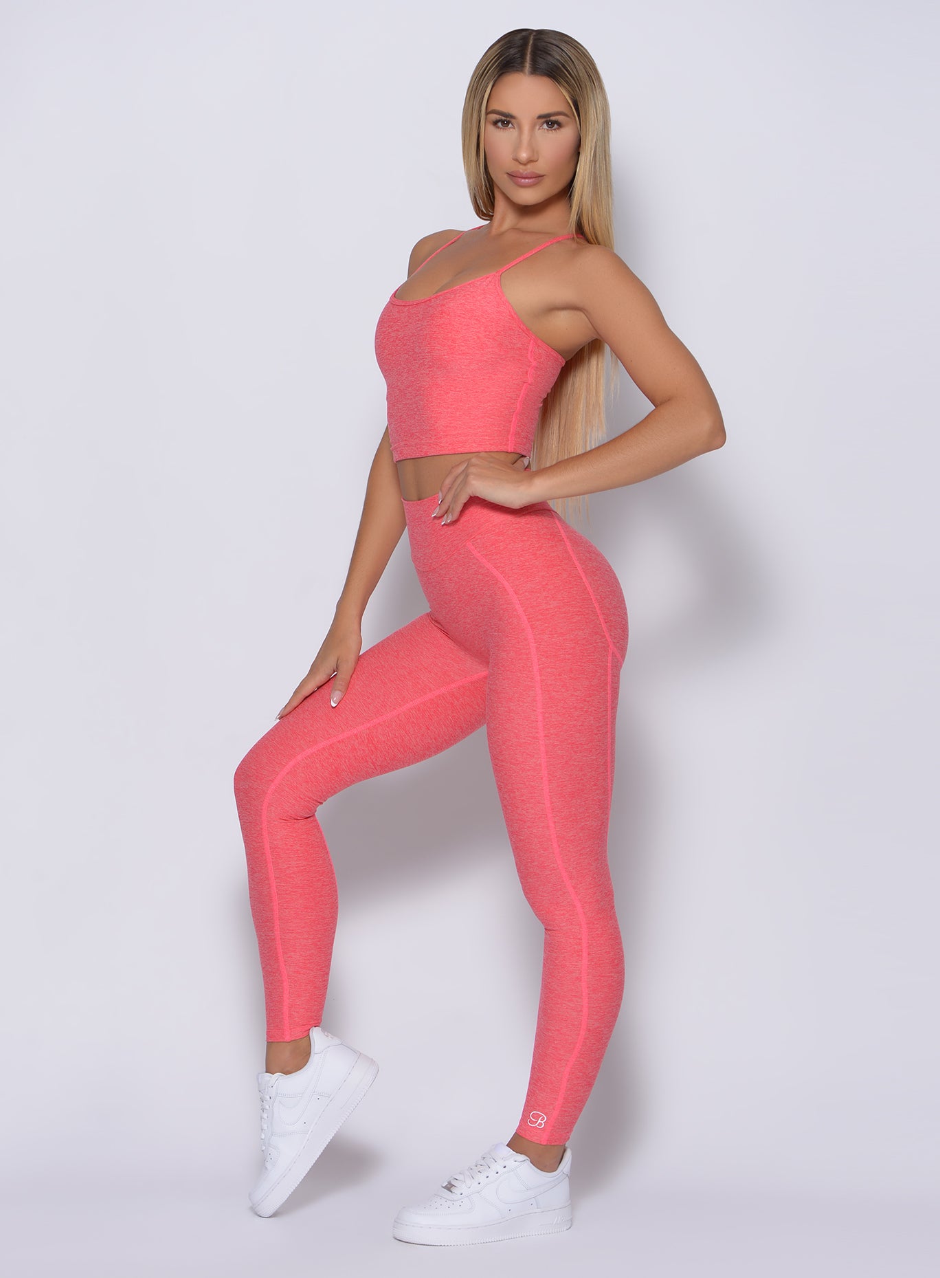 Left side view of the model angled left wearing our uplift leggings in papaya color and a matching bra 