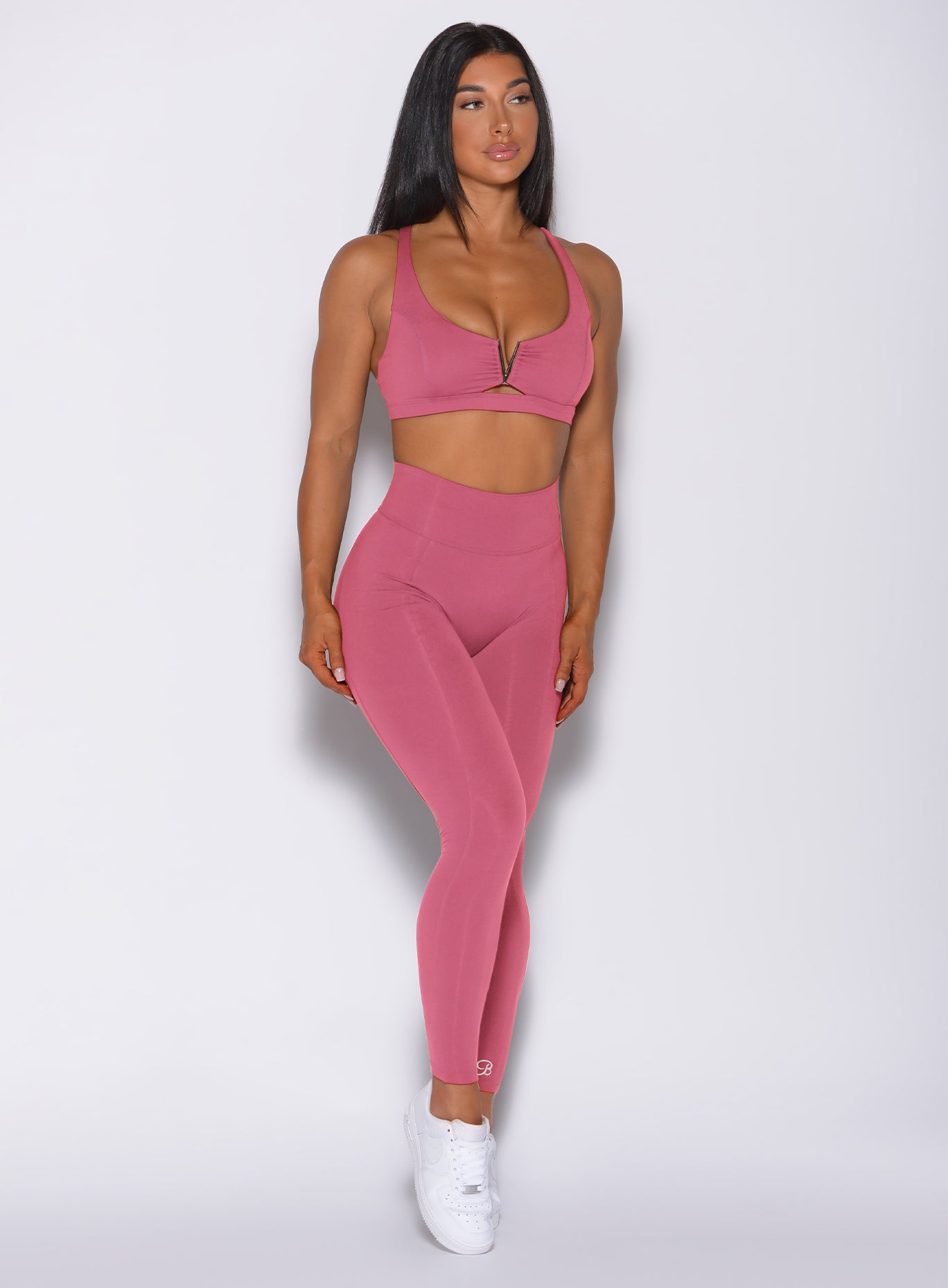 Front profile view of a model in our victory scrunch leggings in blush color and a matching sports bra 