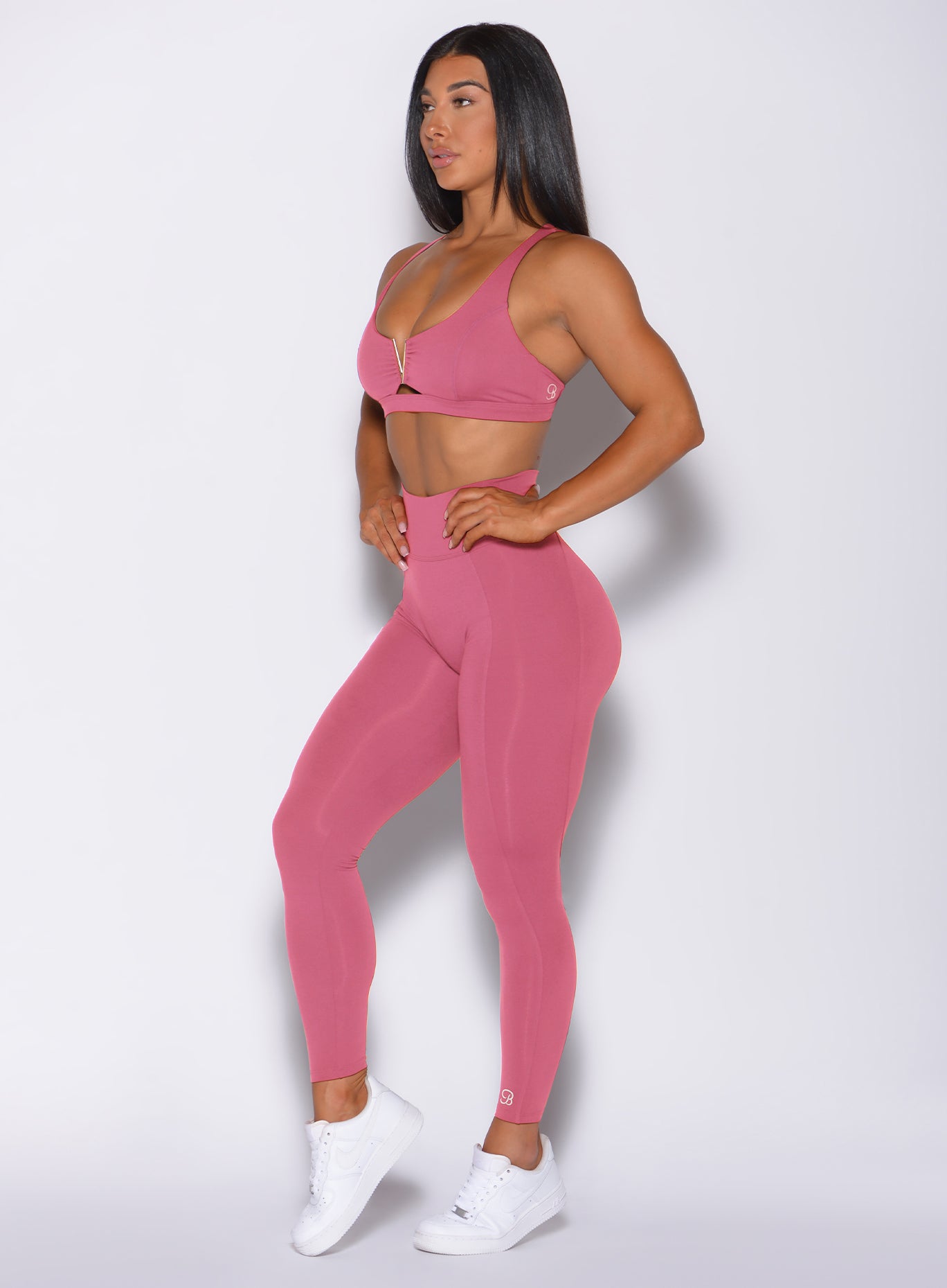 Left side profile view of a model in our victory scrunch leggings in blush color and a matching sports bra