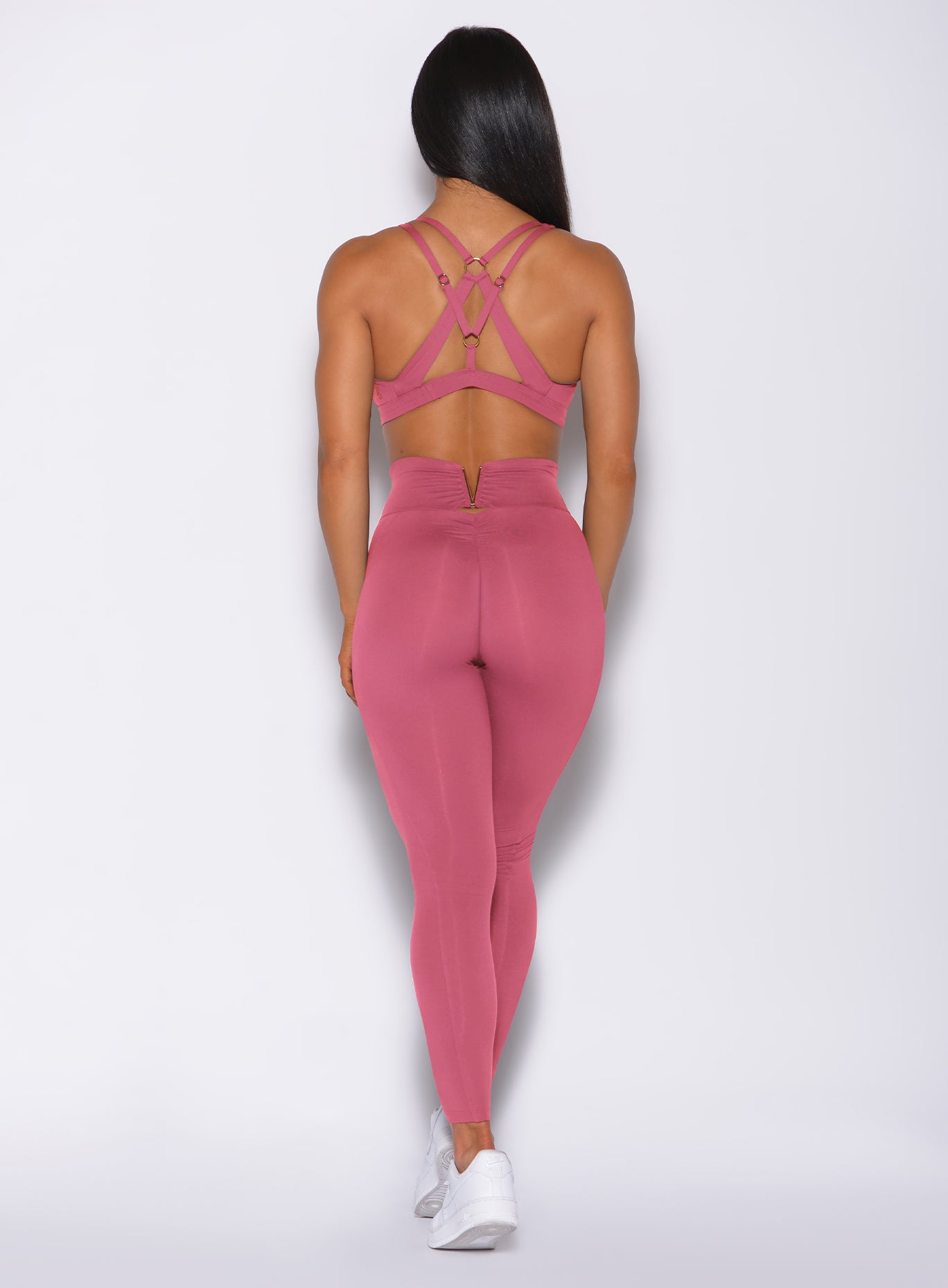 Back profile view of a model in our victory scrunch leggings in blush color and a matching sports bra