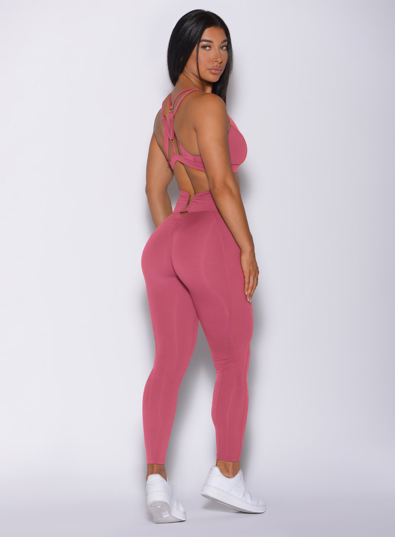 Back side profile view of a model angled slightly to her right wearing our victory leggings in blush color and a matching bra 
