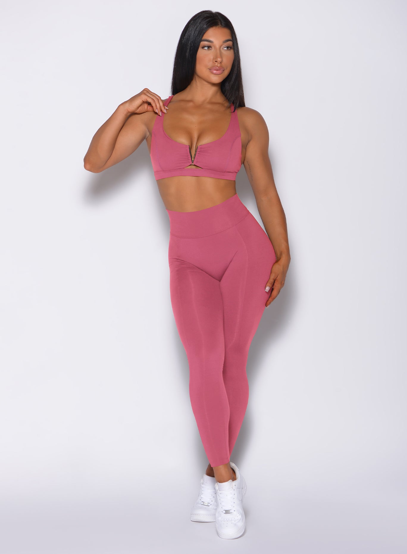 Front profile view of a model wearing our victory scrunch leggings in blush color and a matching sports bra