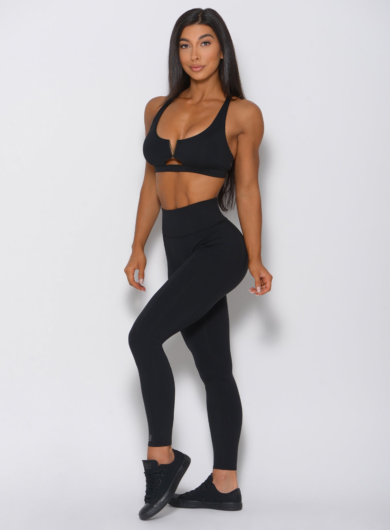 Left side profile view of a model angled left wearing our victory leggings in black and a matching sports bra 