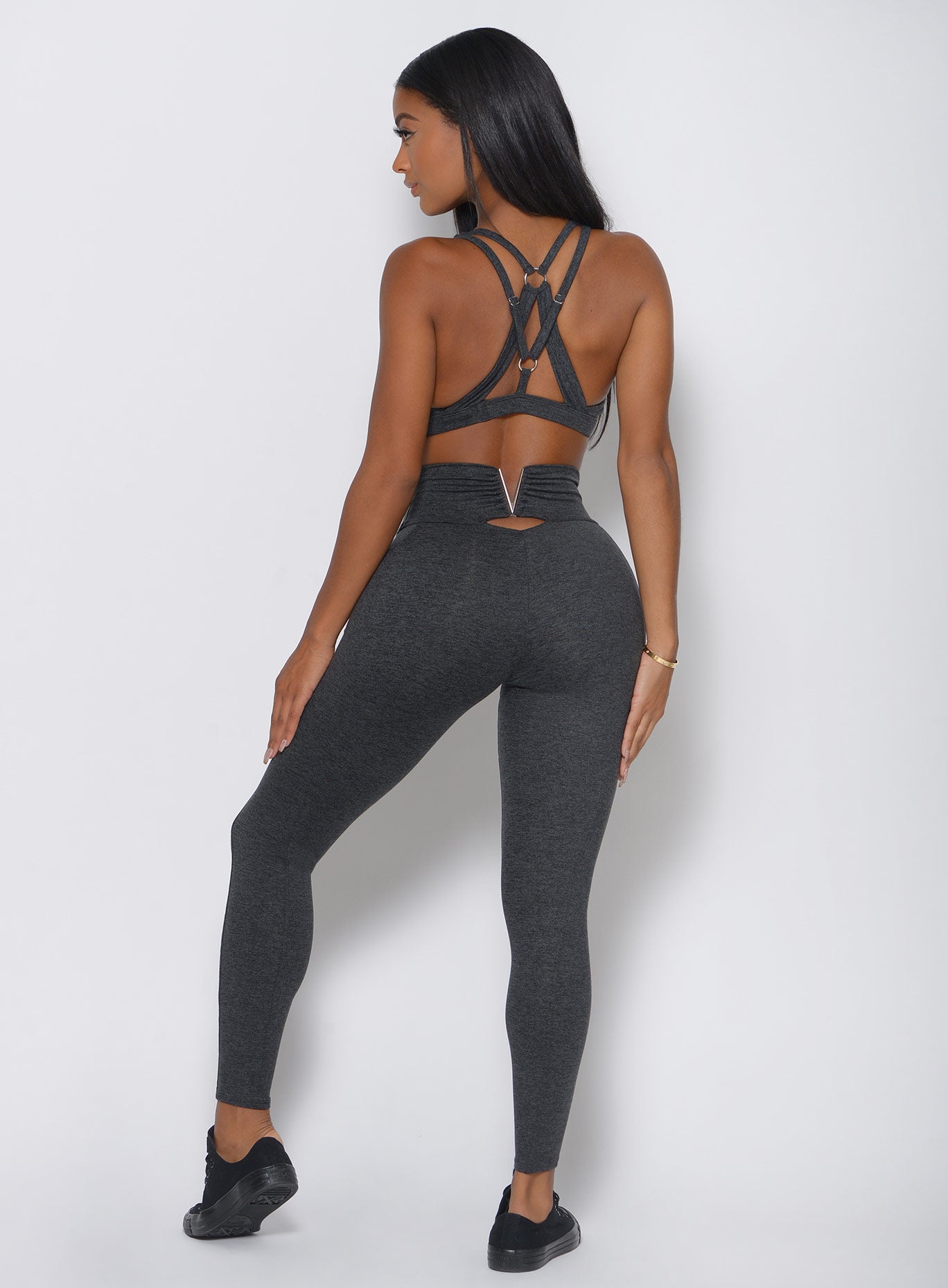 Back view of the model in a high waist gray leggings with a V back design and a matching sports bra 