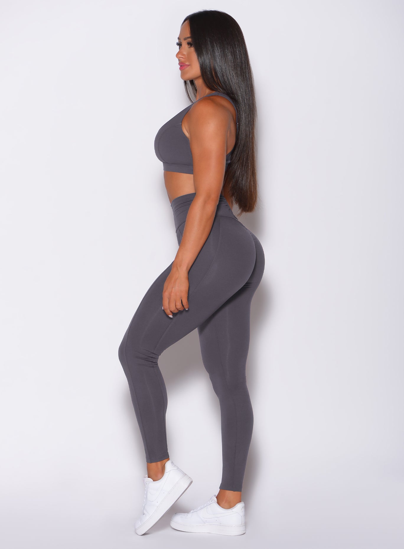 Left side profile view of a model in our victory scrunch leggings in shadow color and a matching sports bra