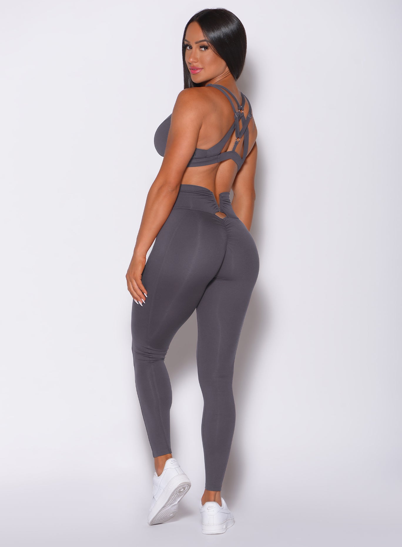 Left side profile view of a model facing to her left wearing our victory scrunch leggings in shadow color and a matching sports bra