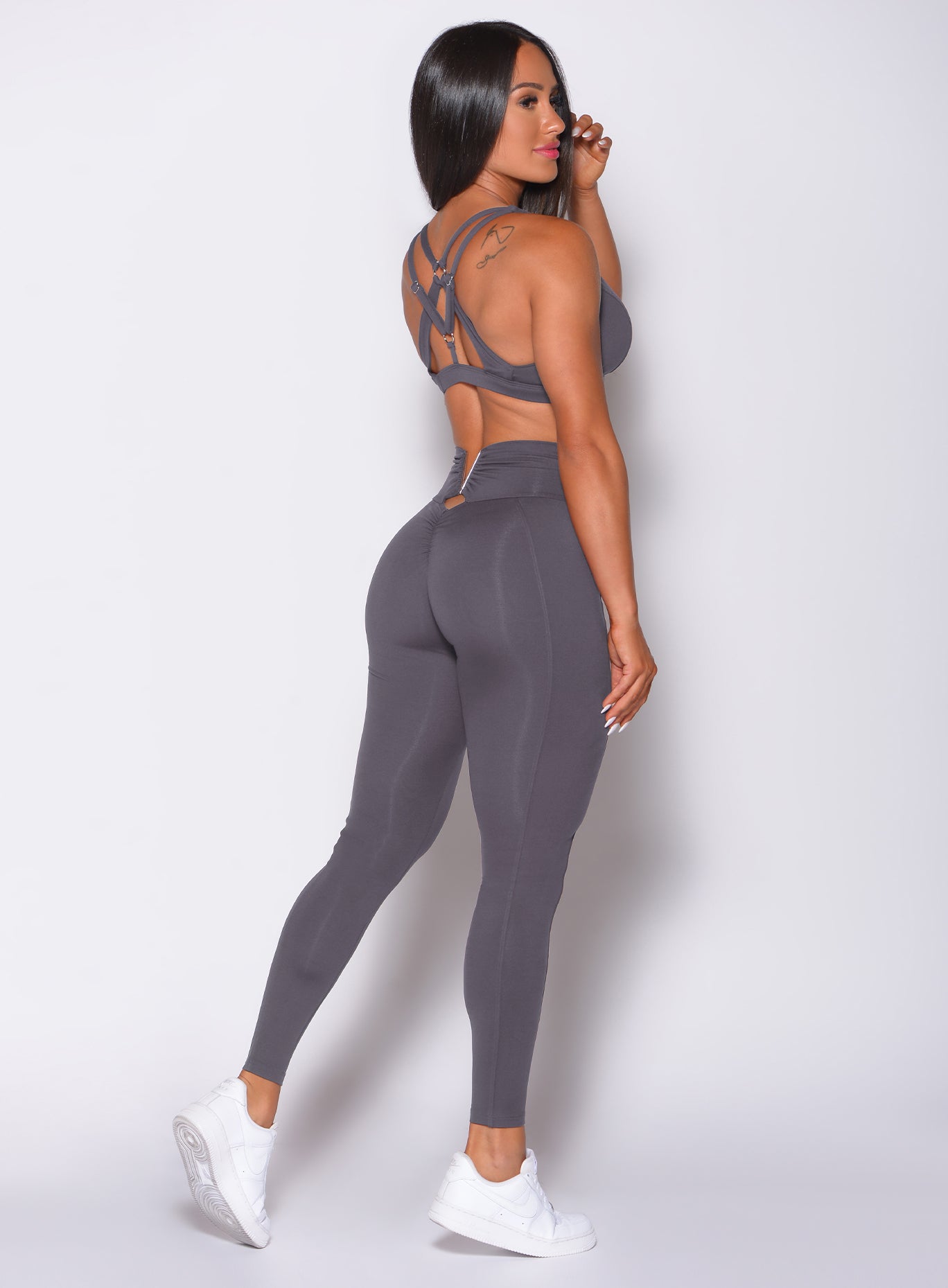 Back profile view of a model wearing our victory scrunch leggings in shadow color and a matching sports bra
