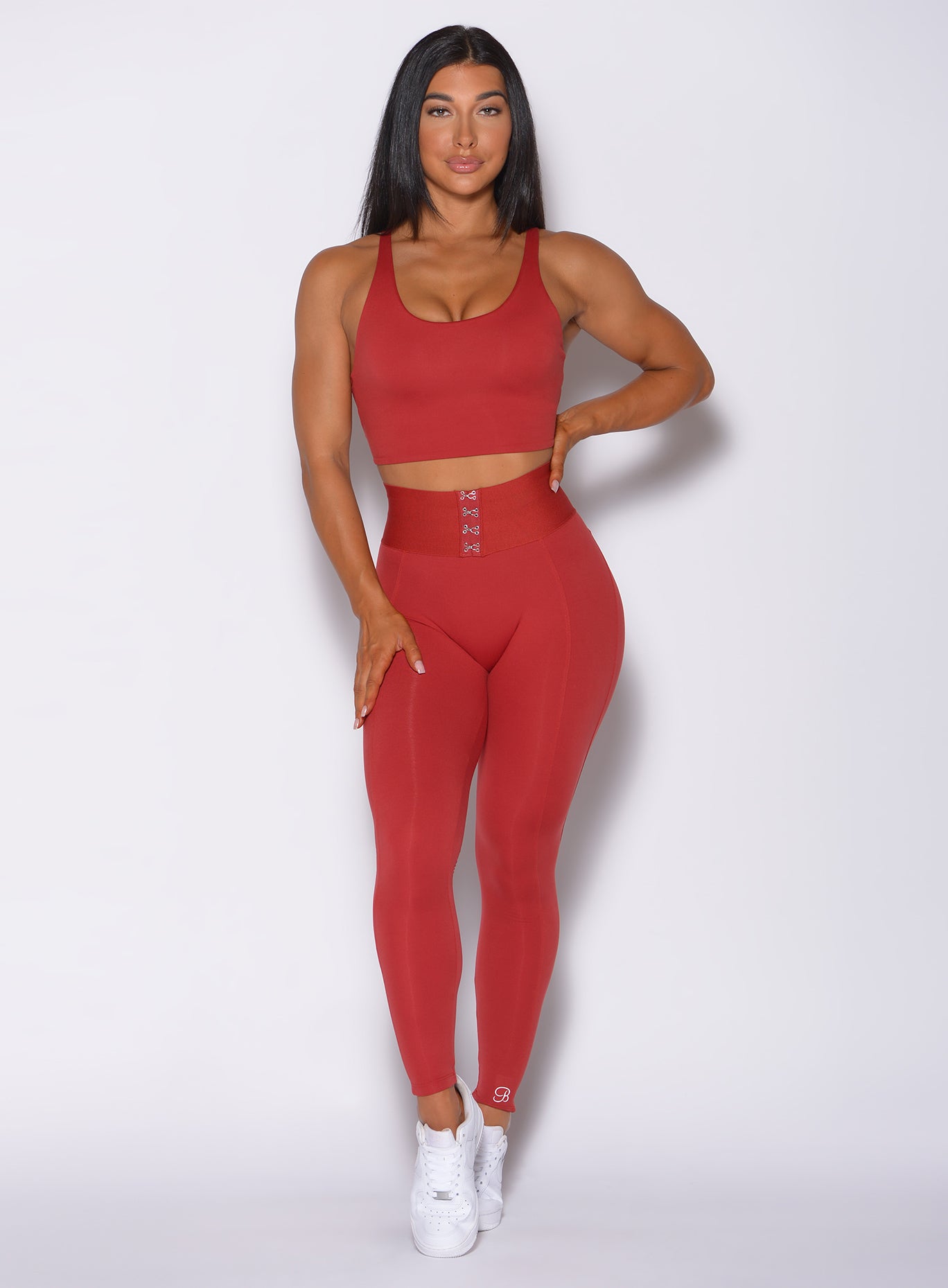 Front  profile view of a model in our waist cincher leggings in sunset red color and a matching sports  bra