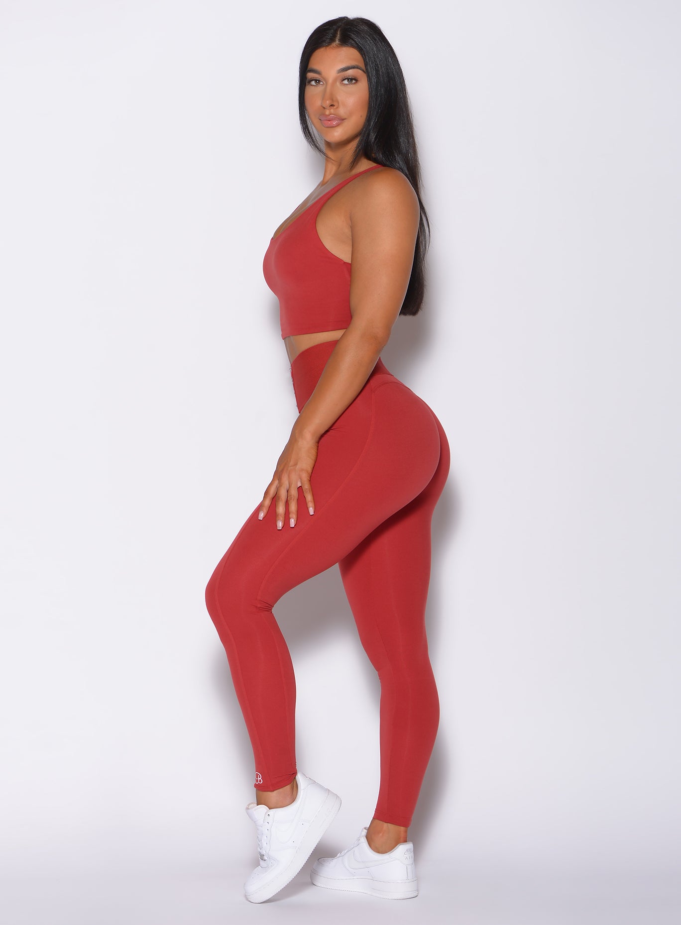 Left side  profile view of a model facing to her left wearing our waist cincher leggings in sunset red color and a matching bra