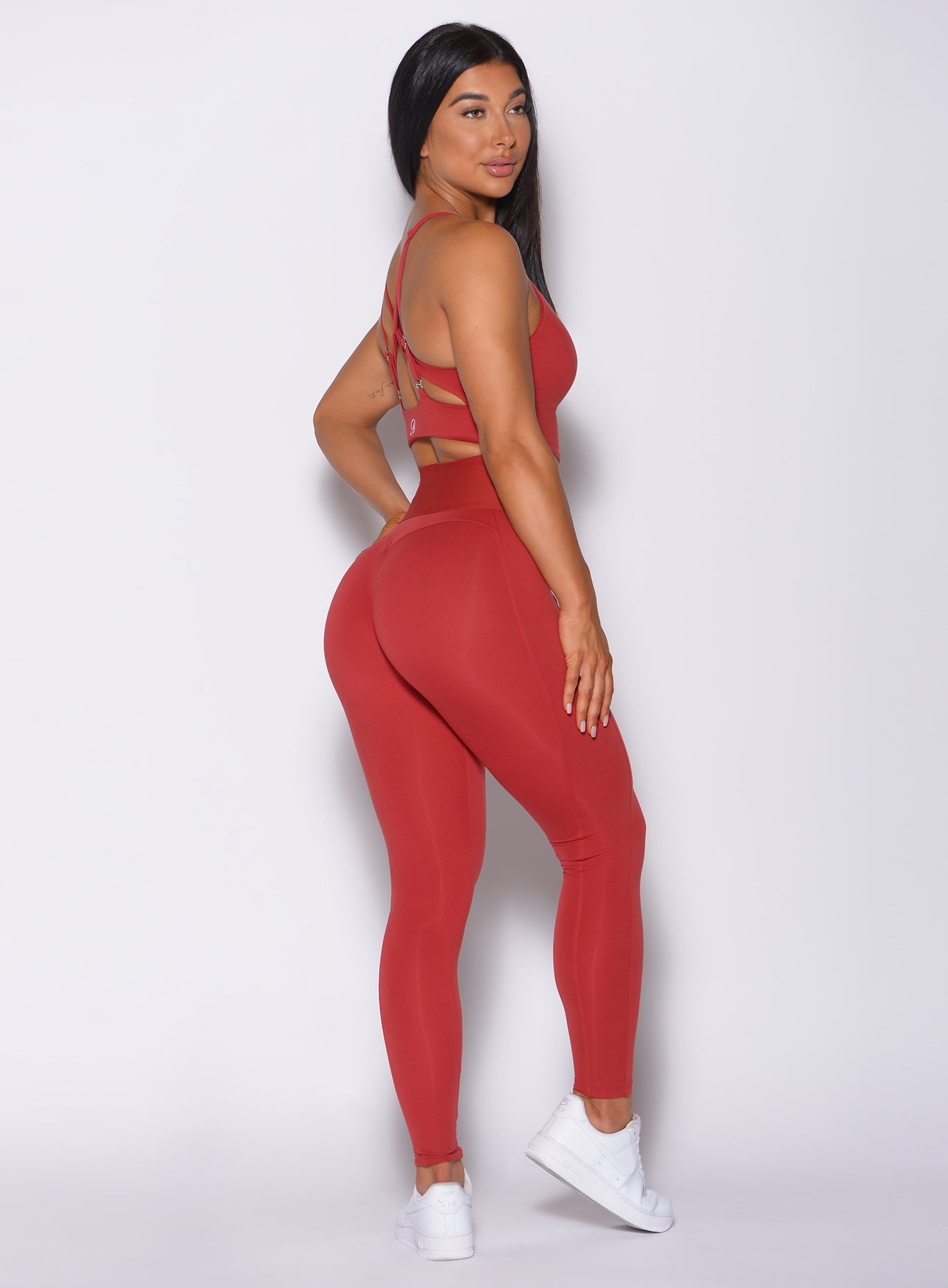 Right side  profile view of a model facing to her right wearing our waist cincher leggings in sunset red color and a matching bra