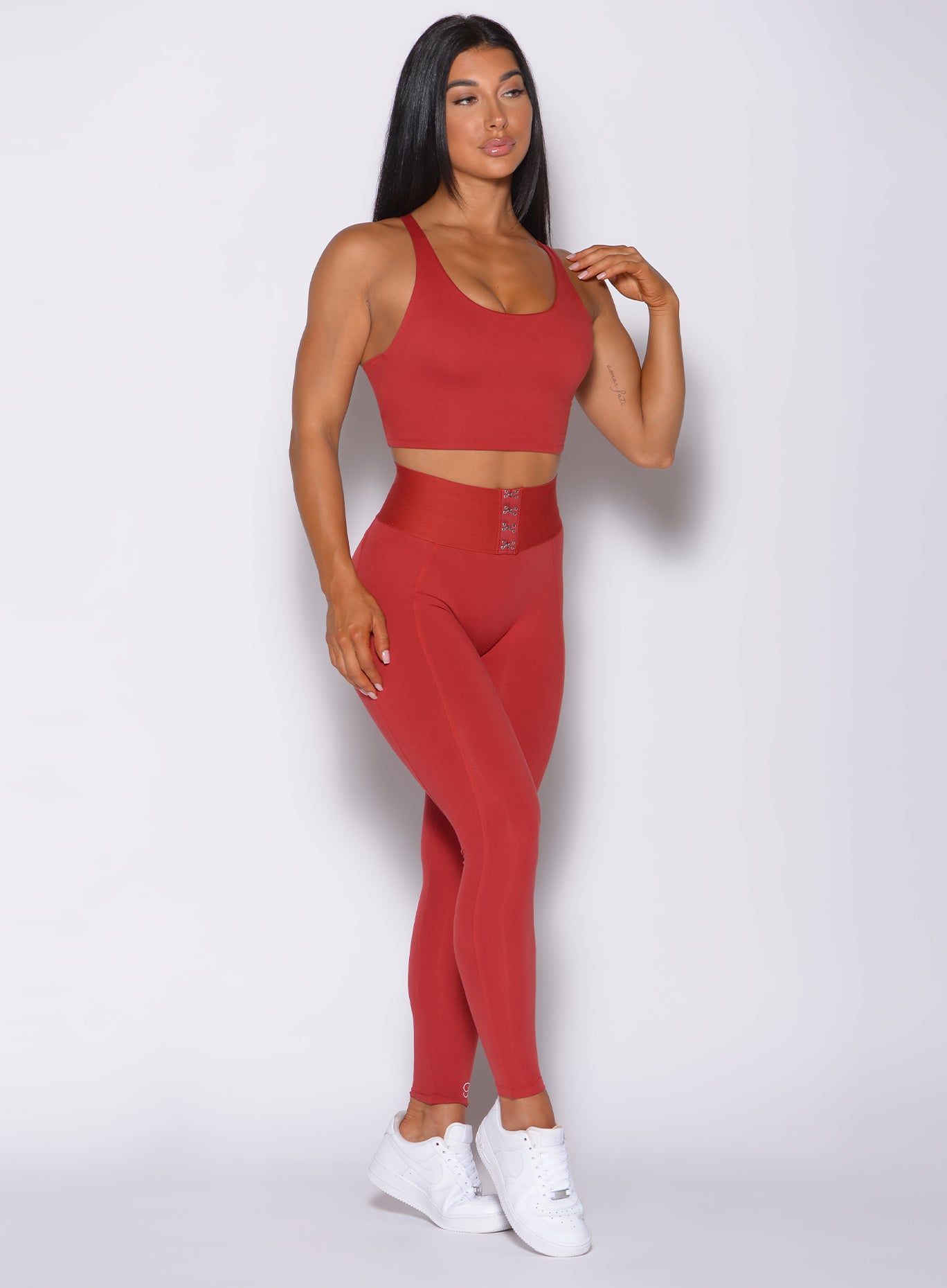 Front  profile view of the model in our waist cincher leggings in sunset red color and a matching sports  bra