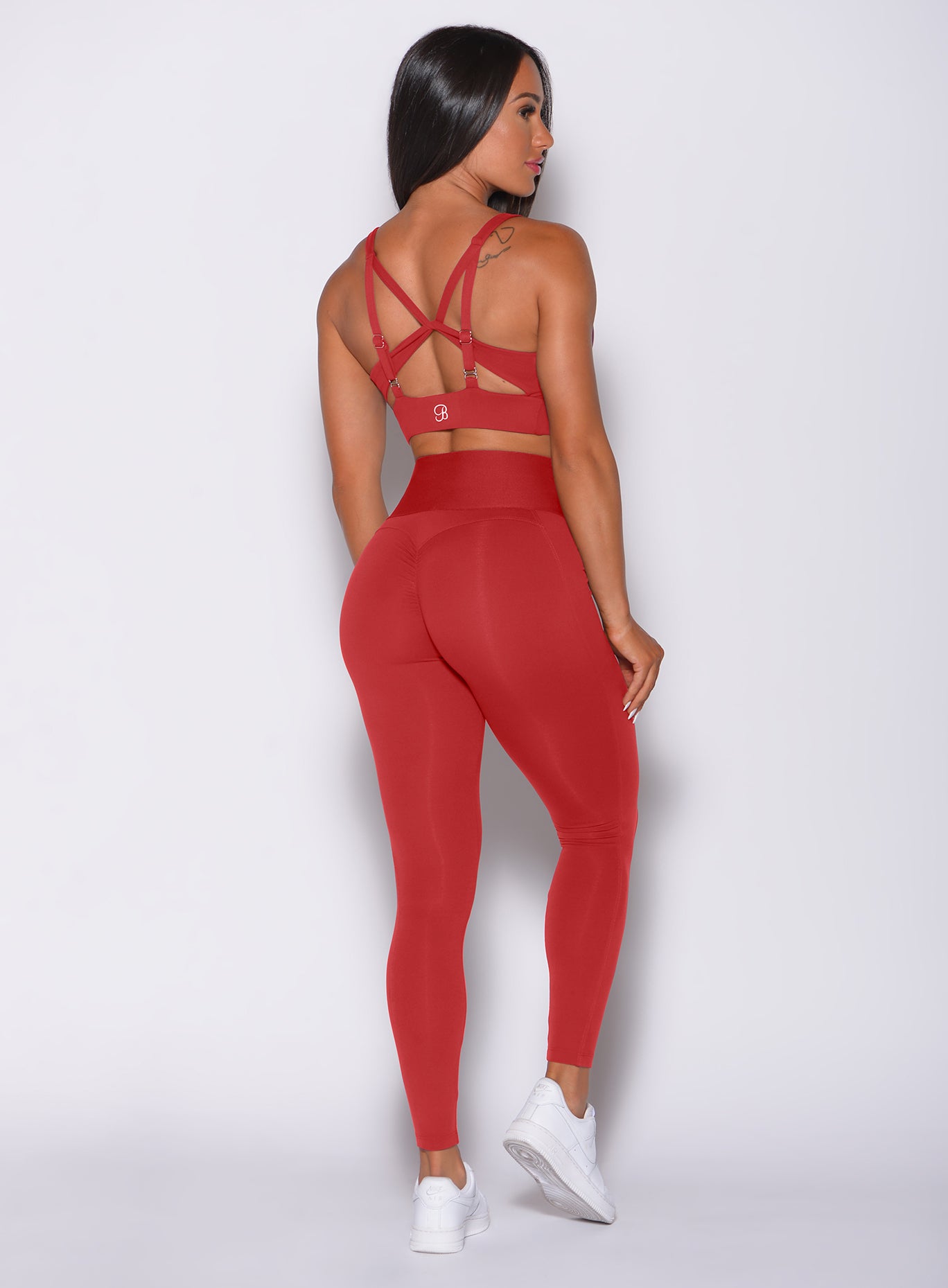 Back profile view of a model facing to her right wearing our impact sports bra in sunset red and a matching leggings