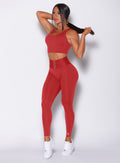 Front profile view of a model holding her hair wearing out impact sports bra in sunset red color and a matching leggings 