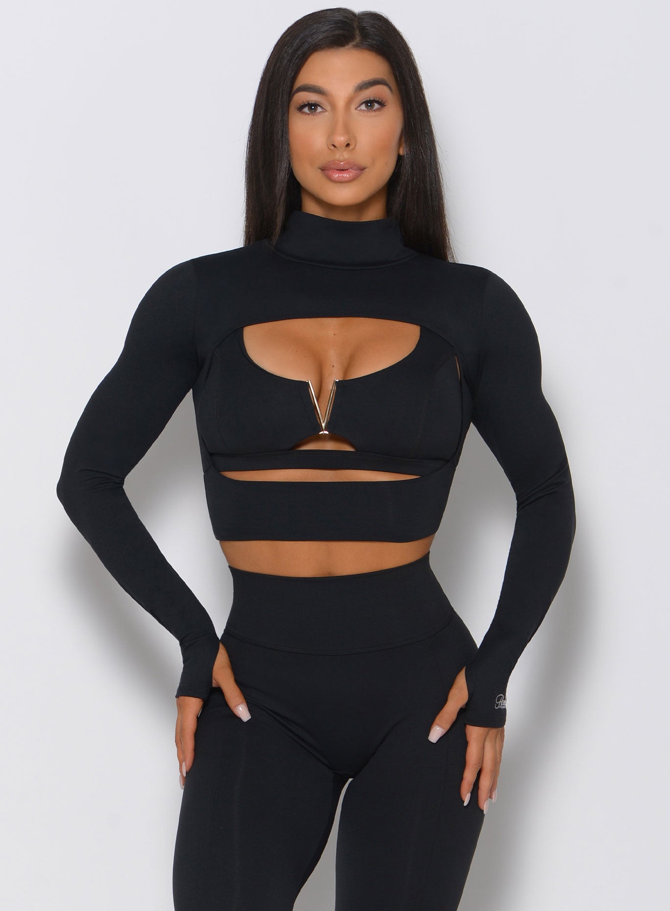 Front facing model in a black sports bra with gold detailing and matching high waist leggings