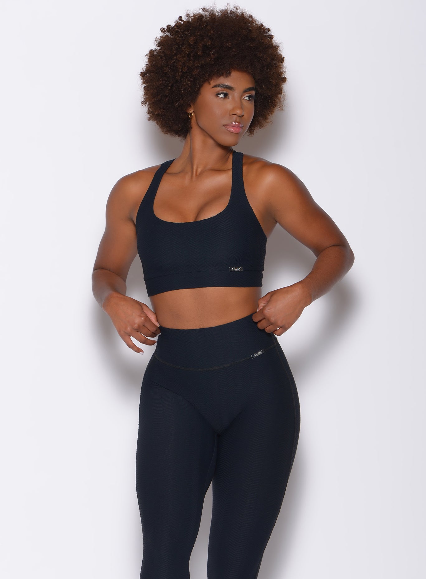 Front profile view of a model facing to her left wearing our chevron sports bra in jet black color and a matching leggings