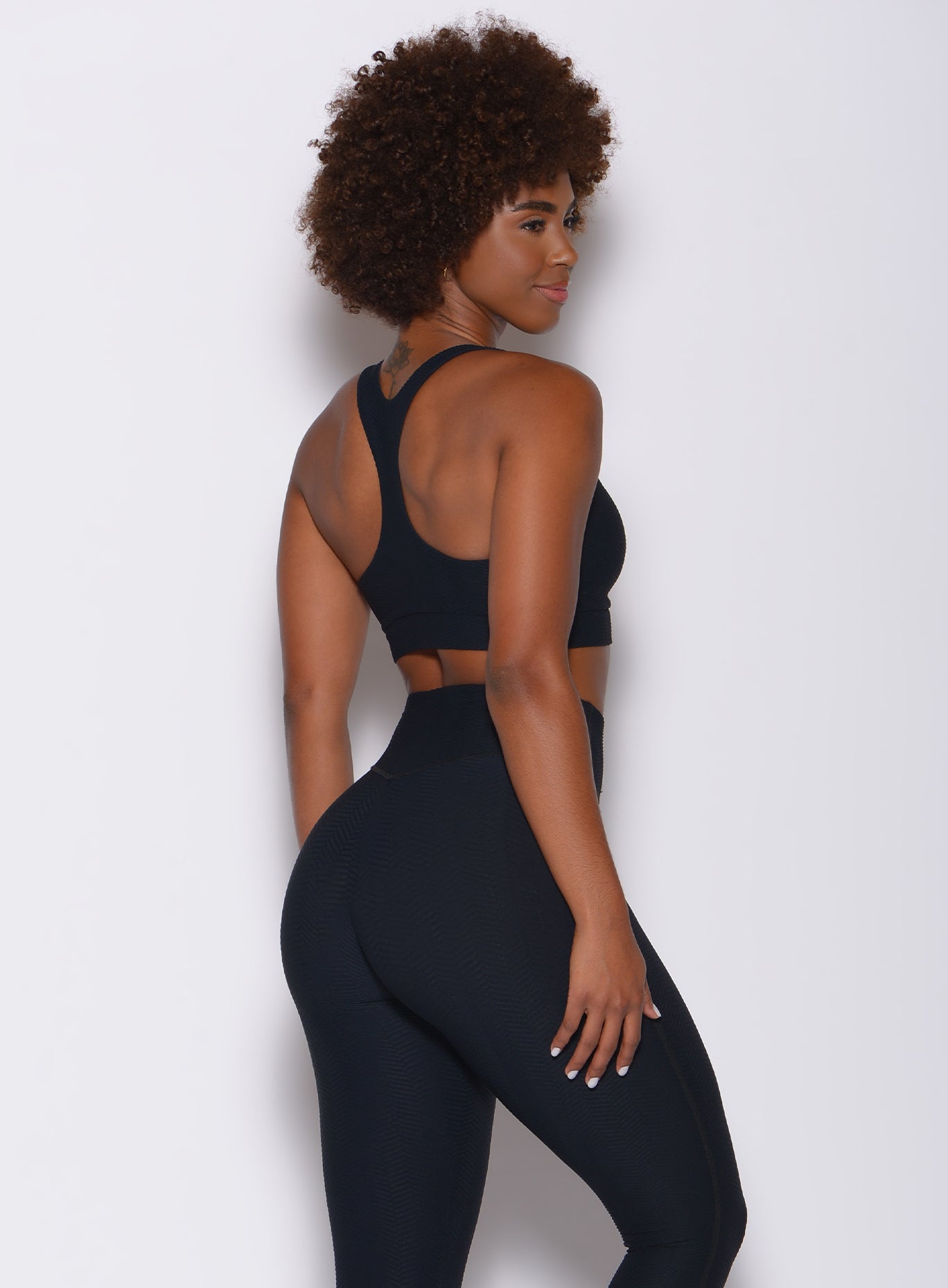 Back profile view of a model in our chevron sports bra in jet black color and a matching leggings