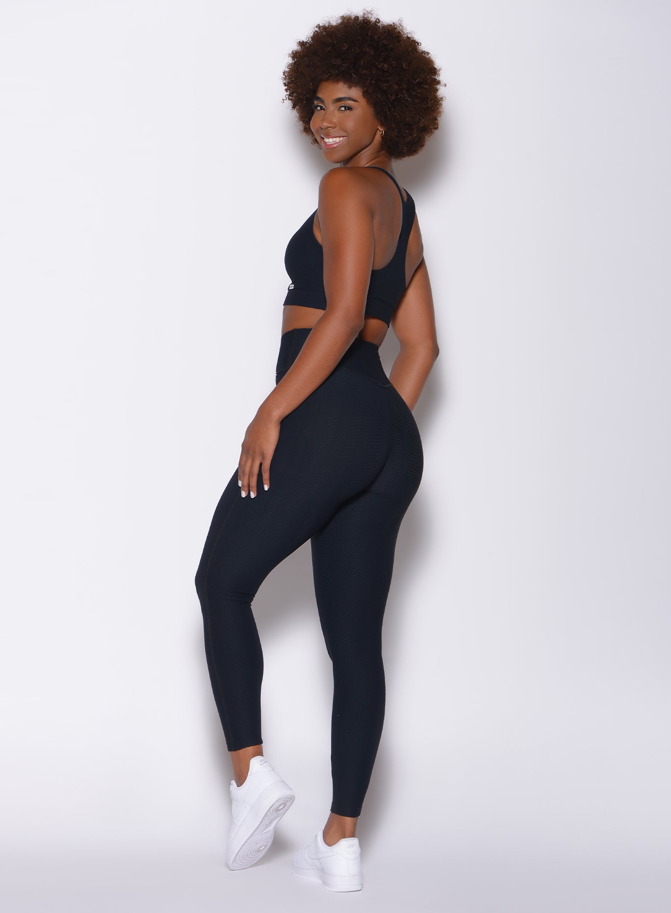 left side profile view of a model in our Chevron Leggings in jet black color and matching sports bra